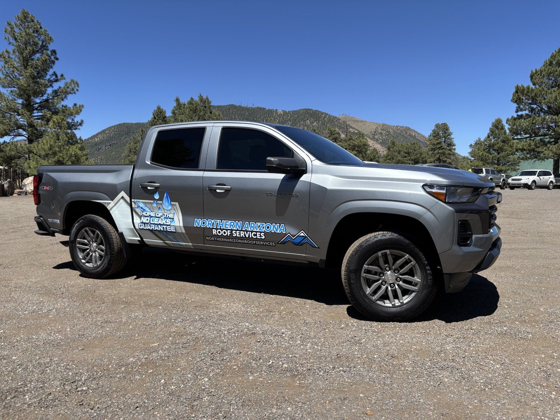 Gray pickup truck with company logo parked on gravel, mountains in the background.