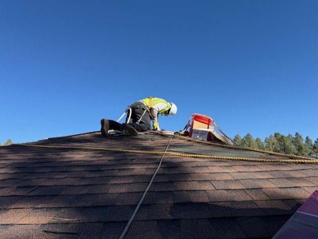 Roofers in safety gear repairing a roof with new orange tiles, on a cloudy day.