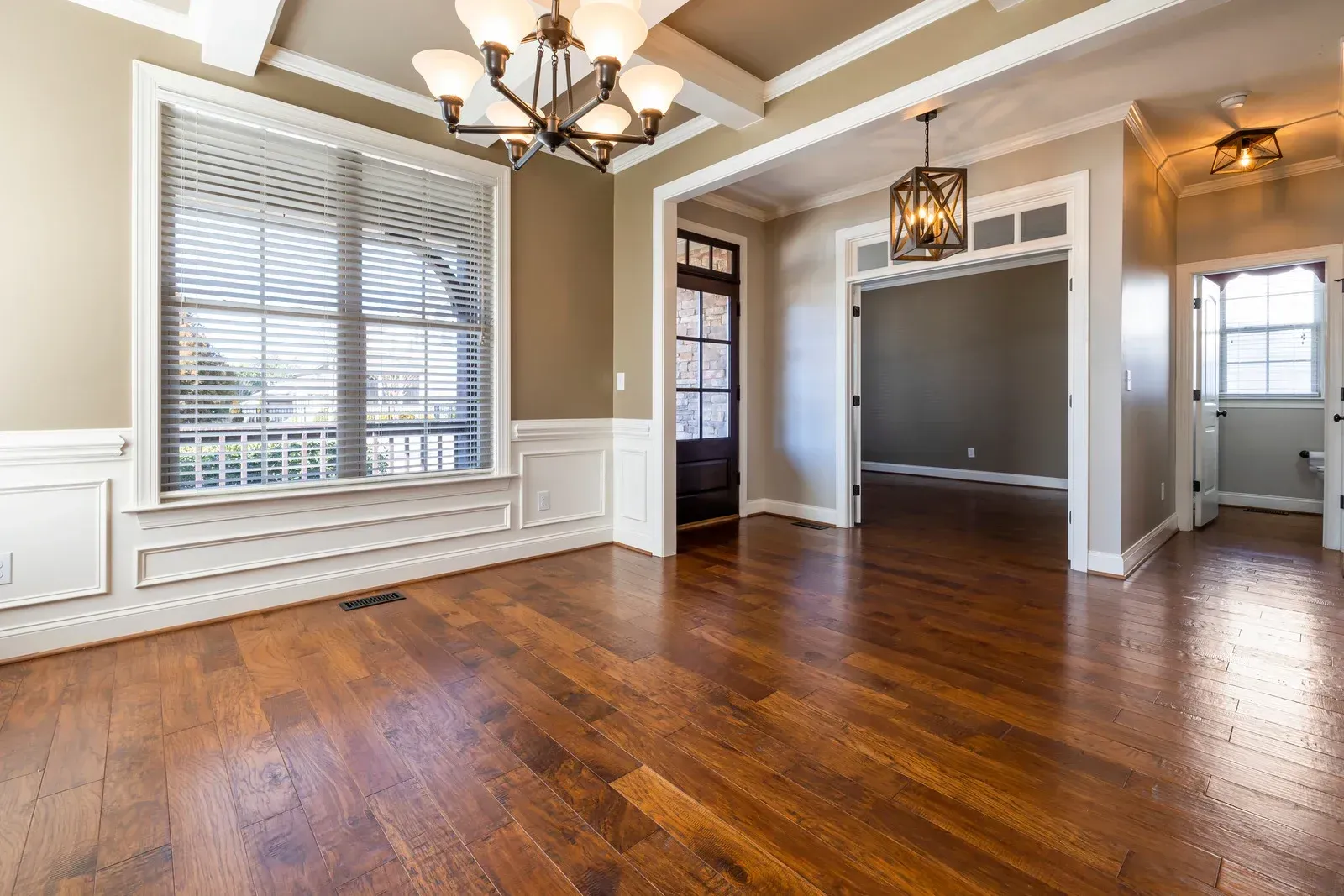 Empty dining room with hardwood floors, brown walls, white trim, and chandelier.