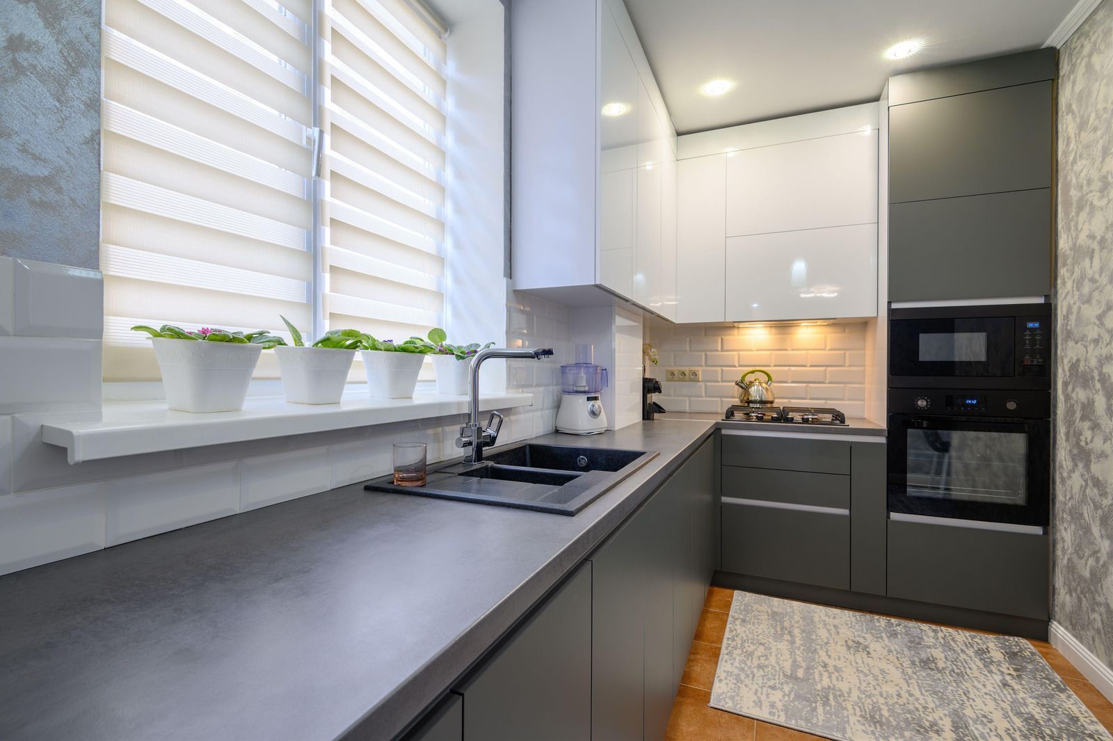 Modern gray and white kitchen with a sink, stove, microwave, and plants on the windowsill.