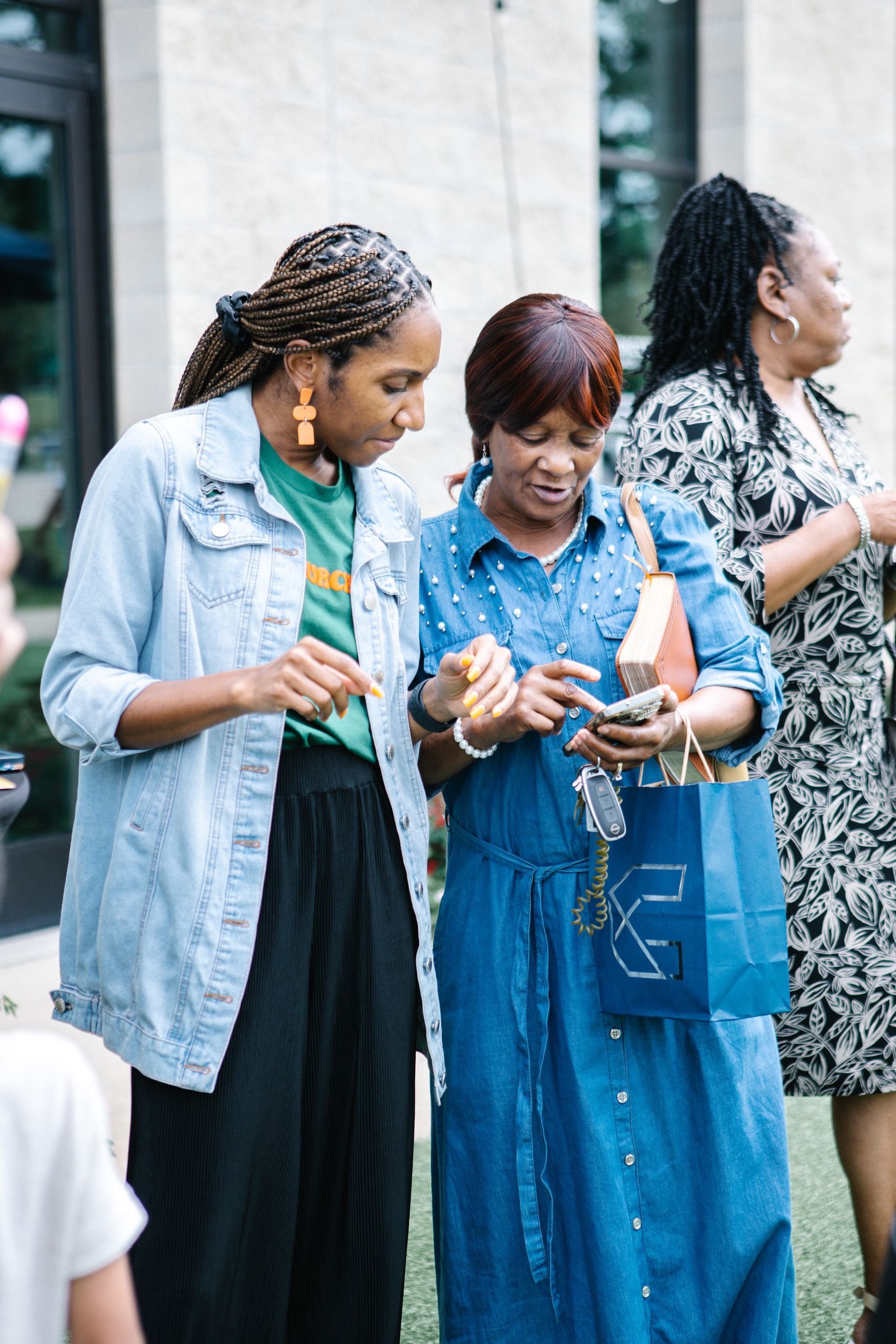 Woman in yellow coat speaks outdoors at a food distribution event, others stand by tables and tents.