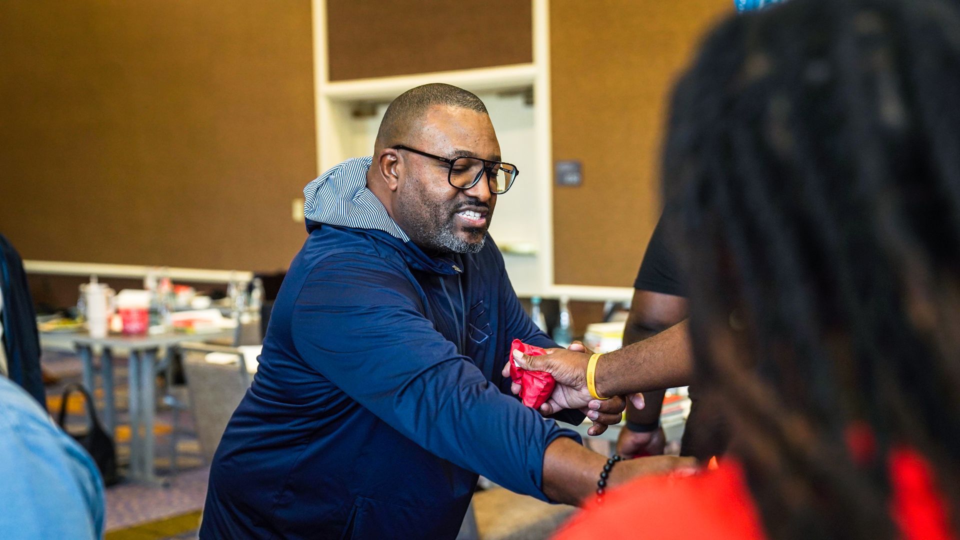 Man in blue shirt gestures, directing outside a truck. Others in masks and shirts.