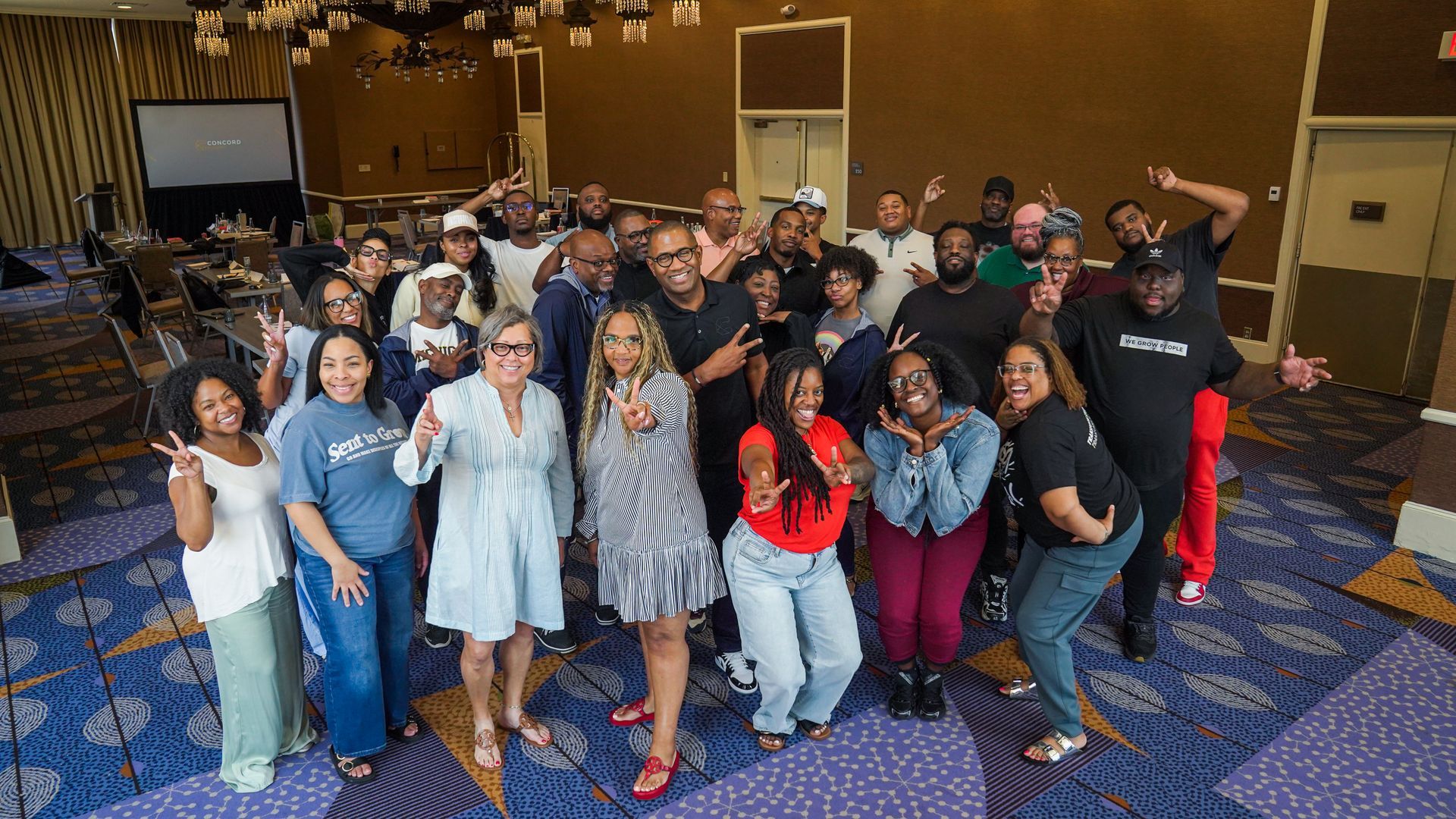 Two women smiling, one holding a phone, the other a gift bag, outside with cars and a building in the background.