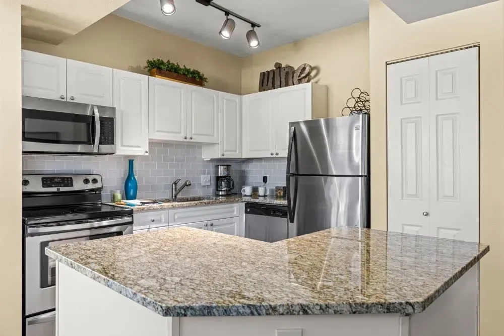White kitchen with granite countertops, stainless steel appliances, and a small island.