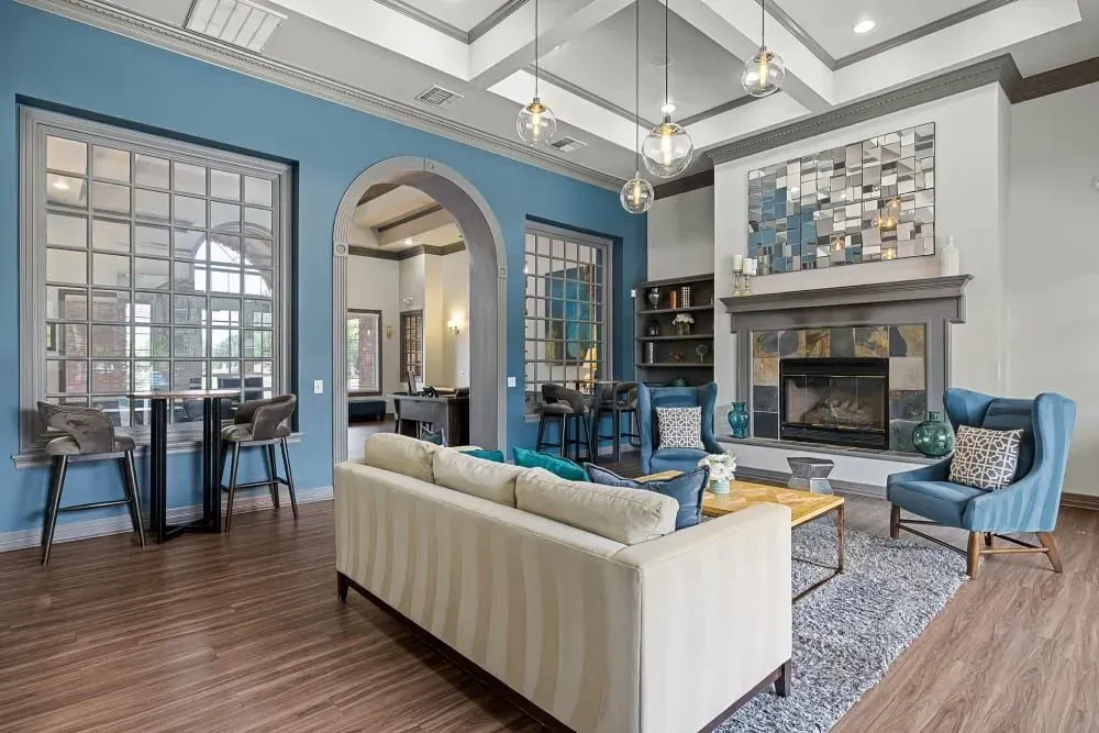 Spacious area with blue walls, fireplace, and a beige sofa, with a bar table and chairs in front of windowed sections.