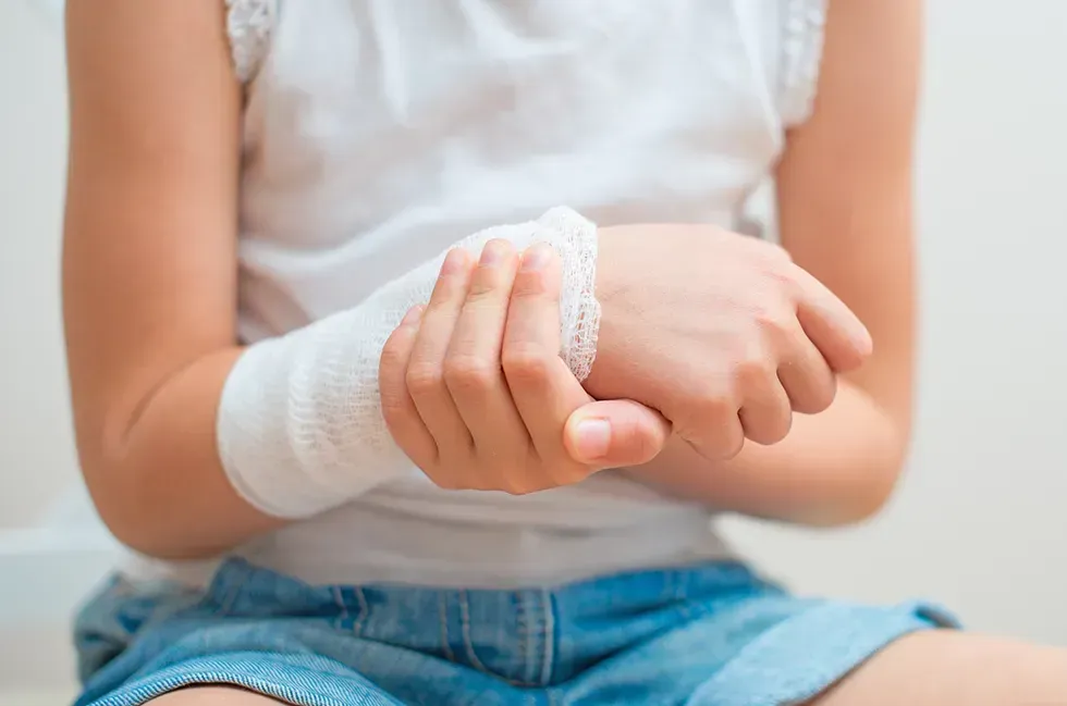 A young girl with a bandaged wrist is sitting on the floor.