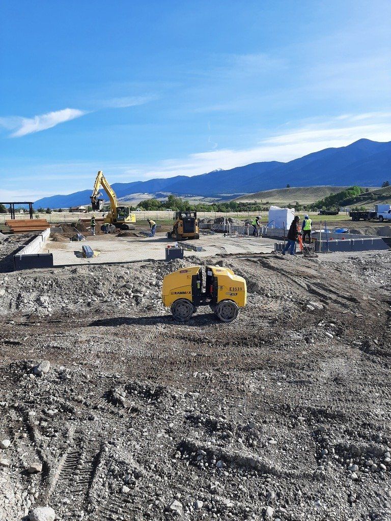A yellow tractor is driving through a dirt field with mountains in the background.