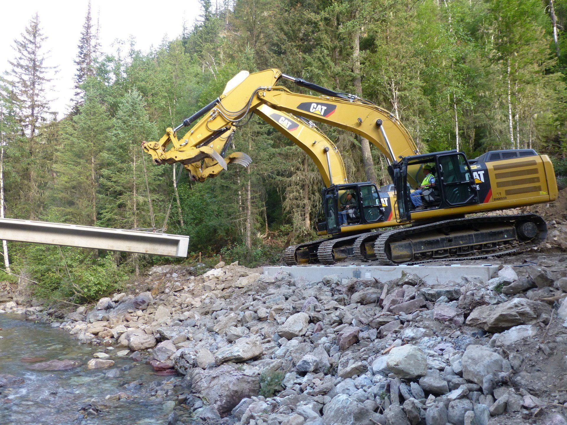 A large excavator is working on a bridge over a river.