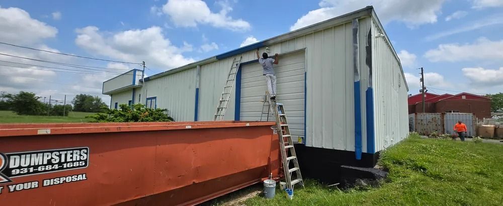 A white building with a red dumpster in front of it.