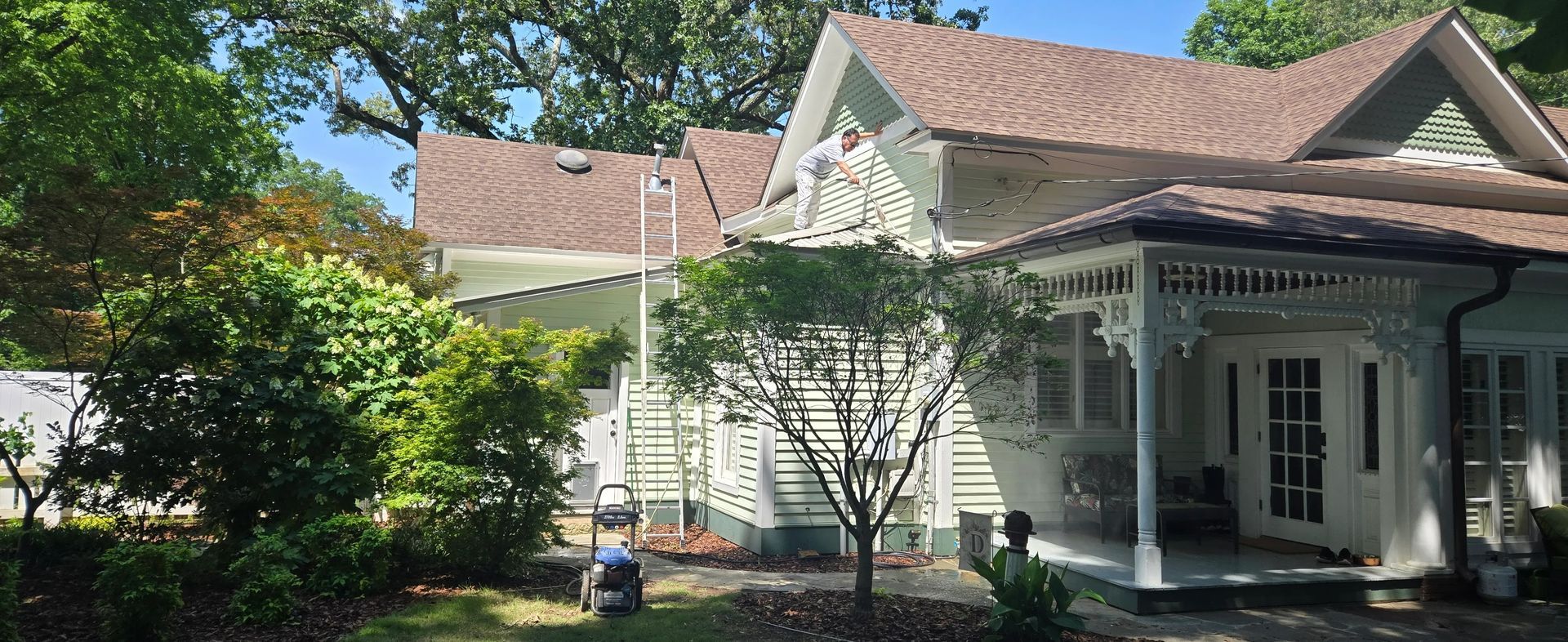A white house with a brown roof is surrounded by trees and bushes.