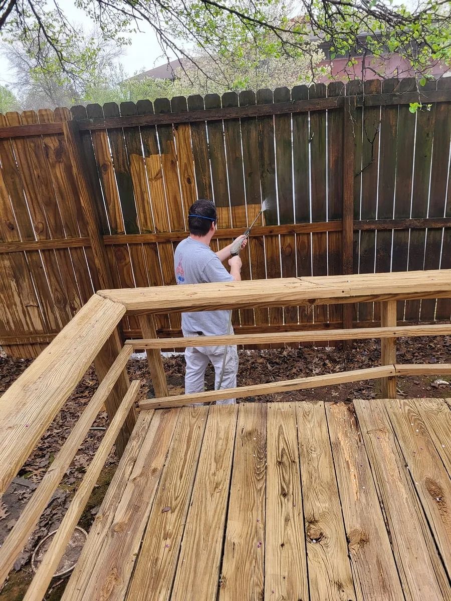 A man is painting a wooden fence on a deck.