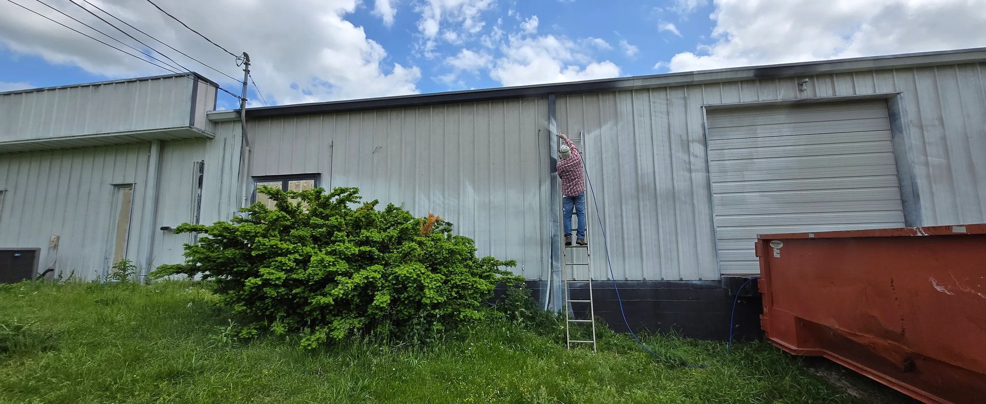 A man is standing on a ladder painting the side of a building.