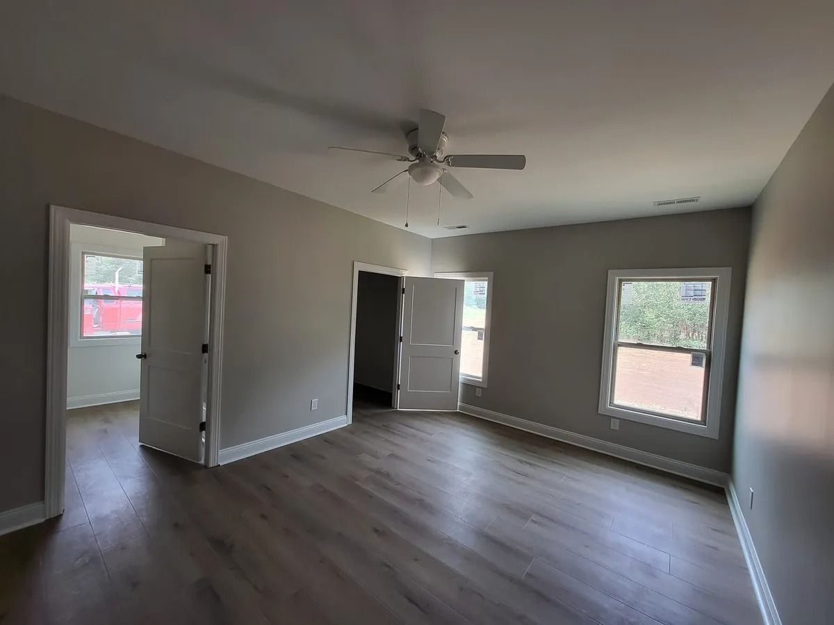 An empty room with a ceiling fan and two windows.