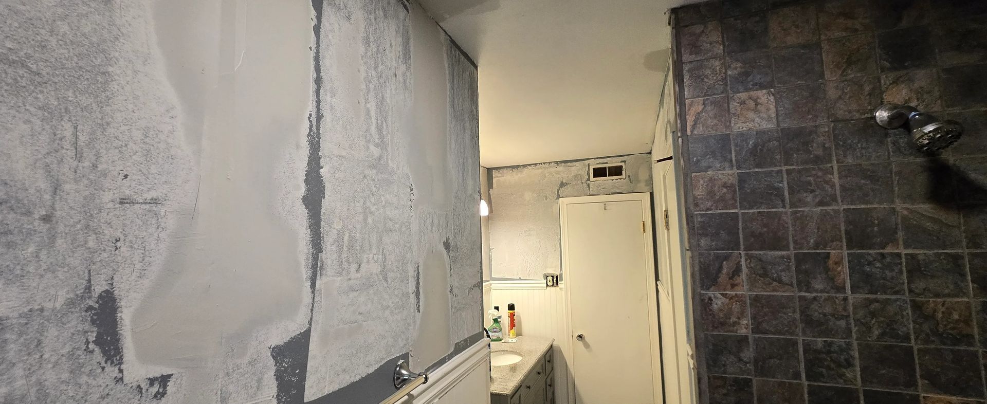 A bathroom with a tiled wall and a shower.