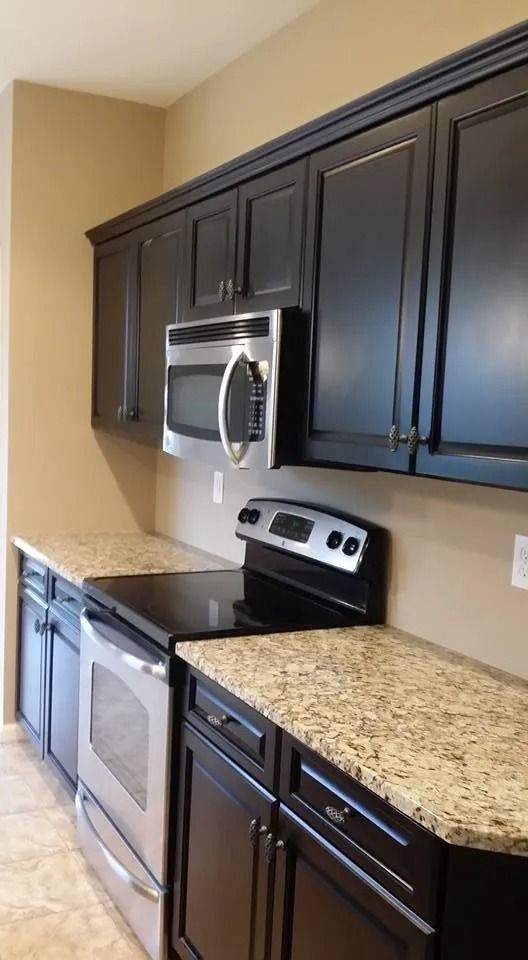 A kitchen with black cabinets , stainless steel appliances and granite counter tops.