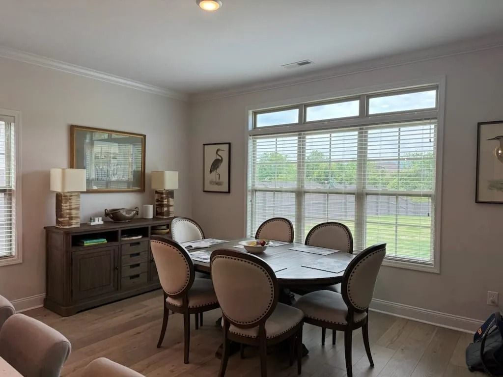 A dining room with a table and chairs in front of a window.