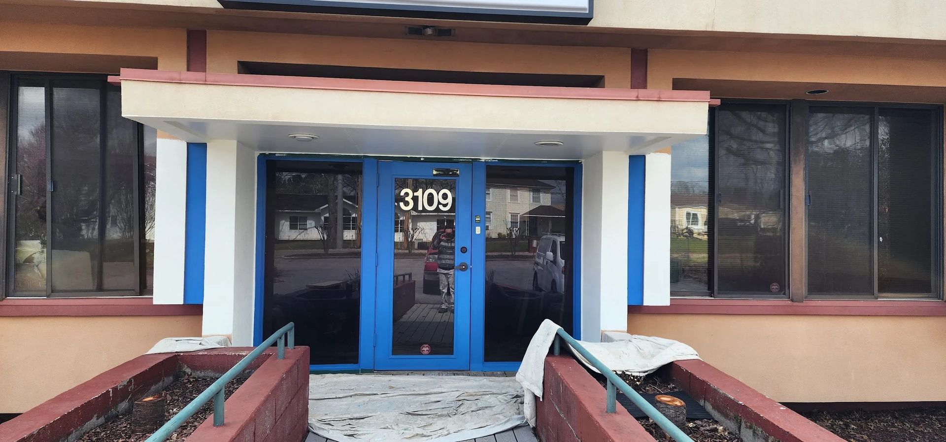 The front of a building with a blue door and a ramp leading to it.