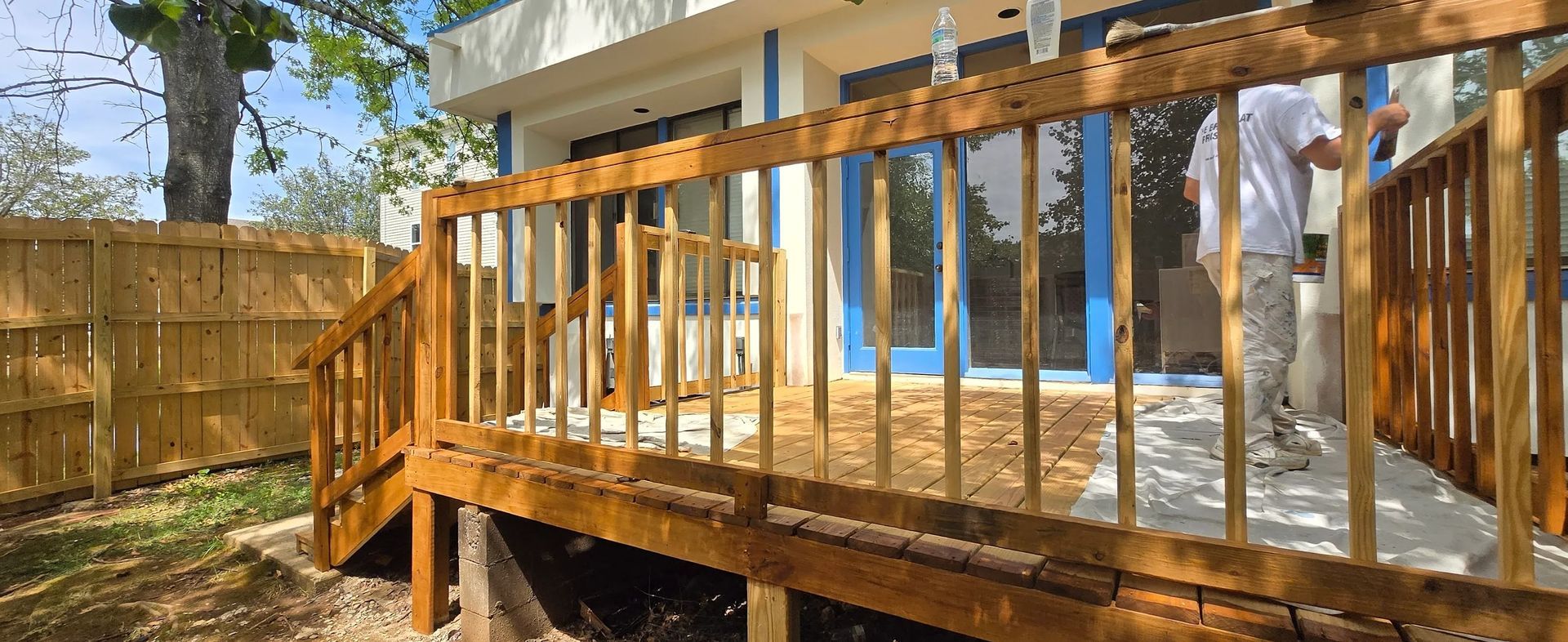 A man is painting a wooden deck in front of a house.