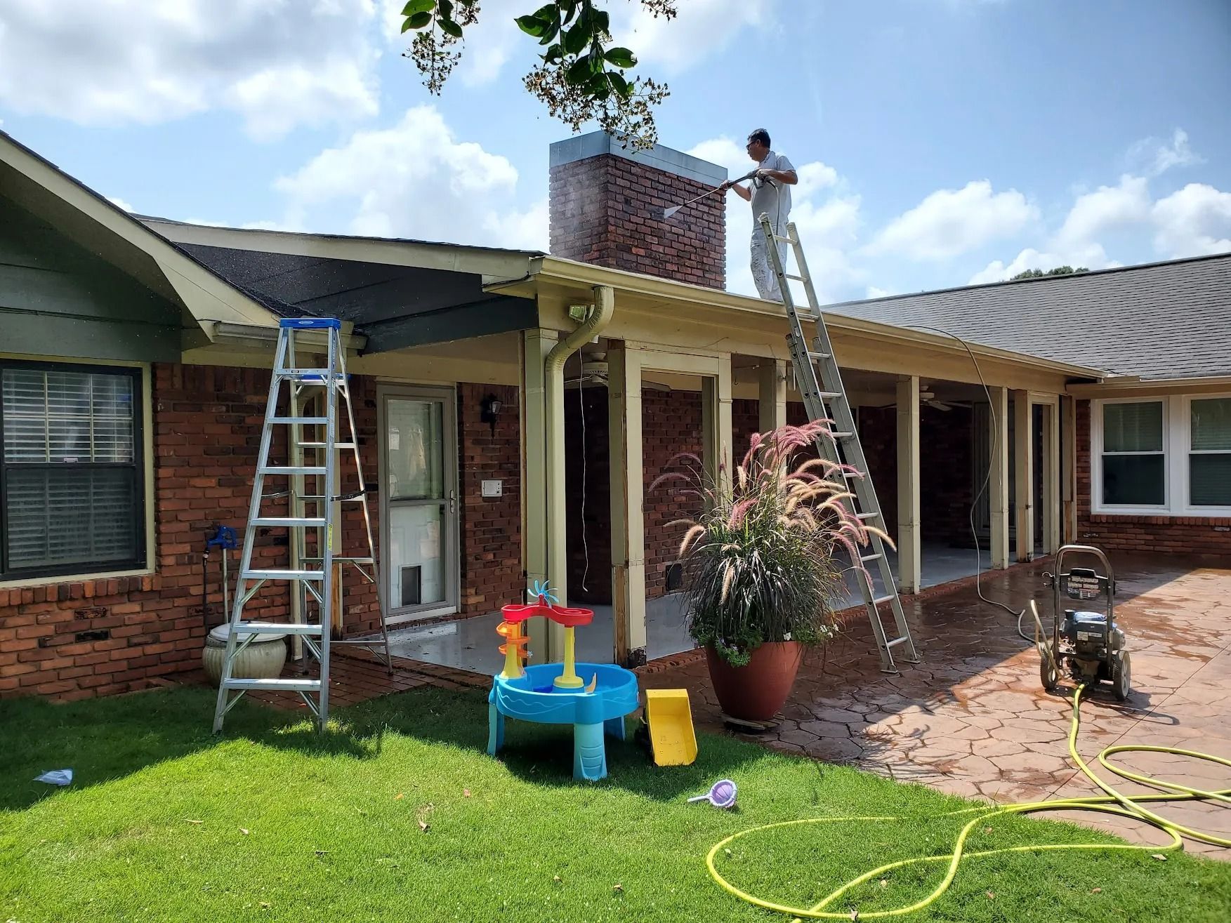 A man is standing on a ladder painting the roof of a house.