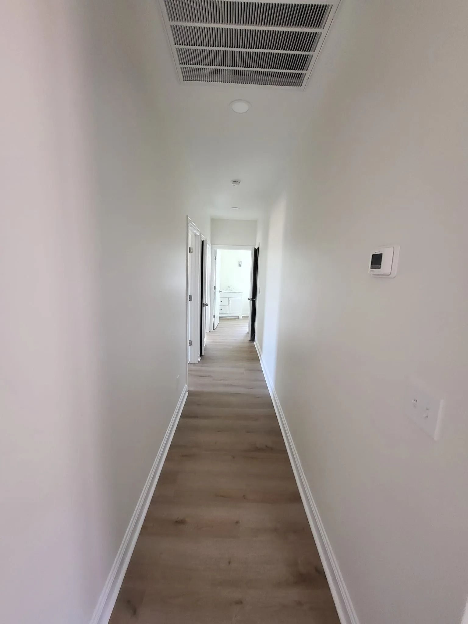 A long hallway with hardwood floors and white walls in a house.