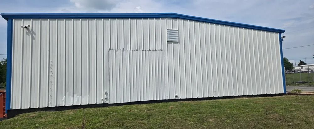 A white metal building with a blue roof is sitting on top of a lush green field.