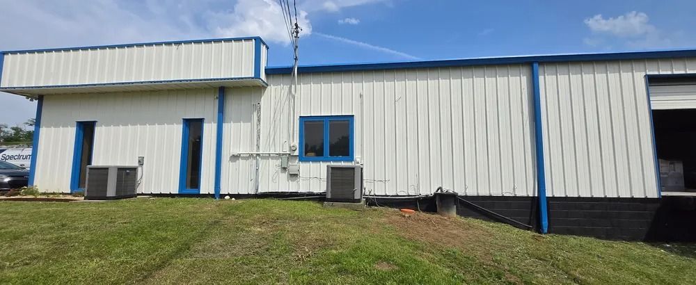 A white building with blue trim is sitting on top of a lush green field.