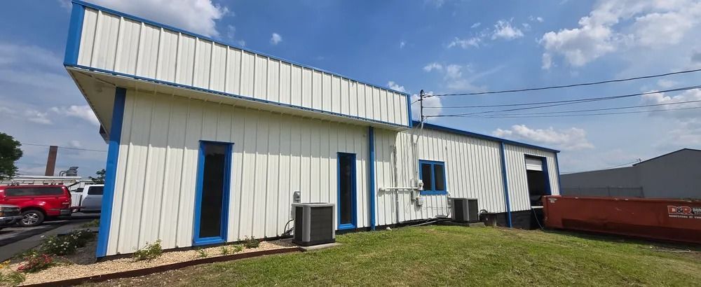 A white building with blue trim is sitting on top of a grassy hill.