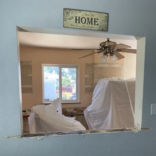 View through an opening in a blue wall into a room under renovation, with a window and covered furniture.