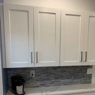 White kitchen cabinets above a backsplash, with a coffee maker on the counter.