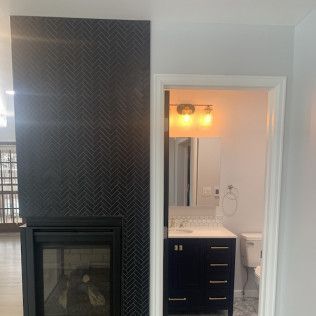 A fireplace with dark tile, next to a bathroom with blue vanity and mirror.