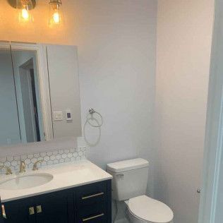 Bathroom with navy blue vanity, white countertop, white toilet, and mirror.