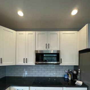 White kitchen cabinets with a stainless steel microwave and gray backsplash.