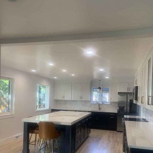 Modern kitchen with white countertops and cabinets, black island, light wood floor, and recessed lighting.