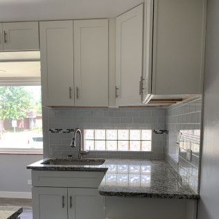 Kitchen with white cabinets, gray backsplash, granite countertop, and a window.