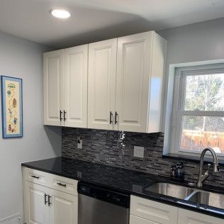 White kitchen cabinets, black countertop, dark backsplash, stainless steel sink.