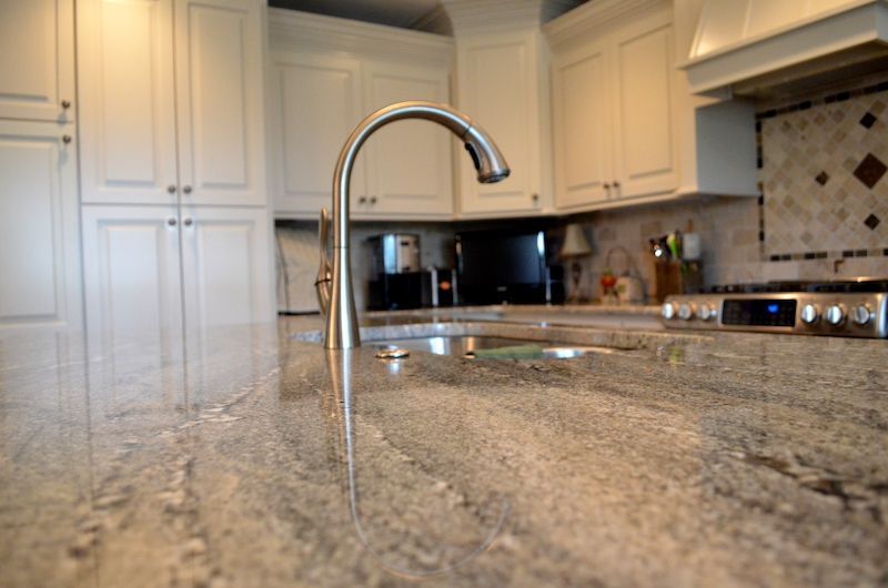 Kitchen interior with granite countertops, stainless steel faucet, and white cabinets.