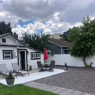 White backyard patio with outdoor furniture, red umbrella, and a white fence.
