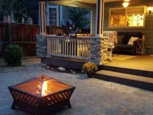 Fire pit on patio with lit flames, covered porch in background, nighttime.