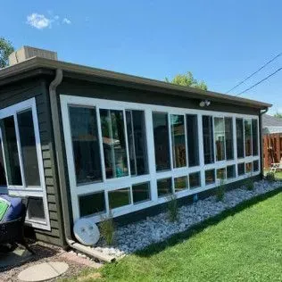 Sunroom with many windows, green siding, and white trim against a blue sky.
