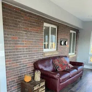 Red brick wall with burgundy leather couch, windows, and small wooden table.