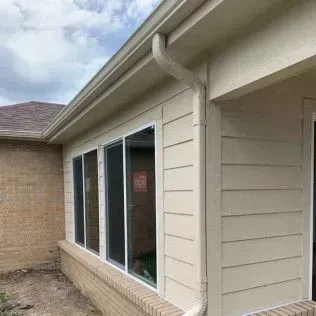 Beige siding and trim on a house, with windows, a gutter, and a brick foundation.