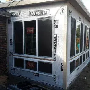 A sunroom addition under construction, with Everbilt windows and tarp paper.