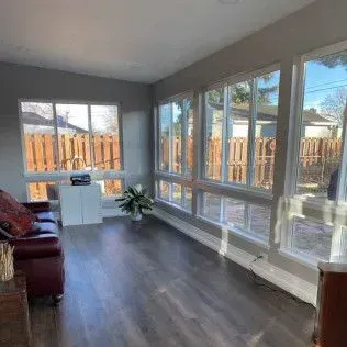 Sunroom with large windows, dark flooring, and a red leather sofa.
