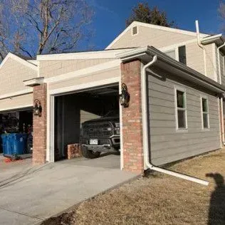 Two-car garage with brick accents; a truck is inside one bay. Tan siding and a blue sky.