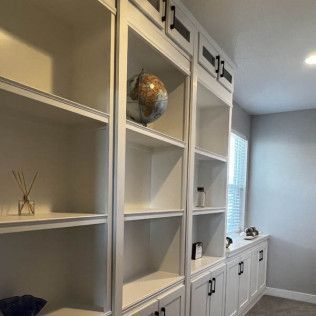 White built-in bookshelves with black hardware; a globe and a few small items sit on shelves, beside a window.