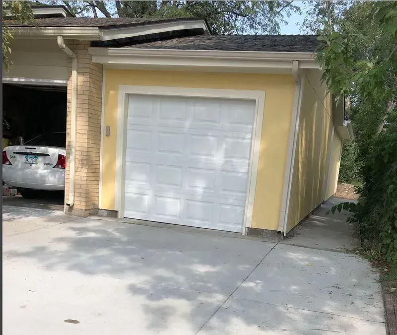 Yellow garage with white door and adjacent driveway, car in open garage on left.