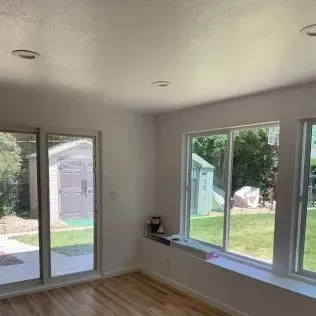 Empty room with windows overlooking a backyard and sliding glass door.