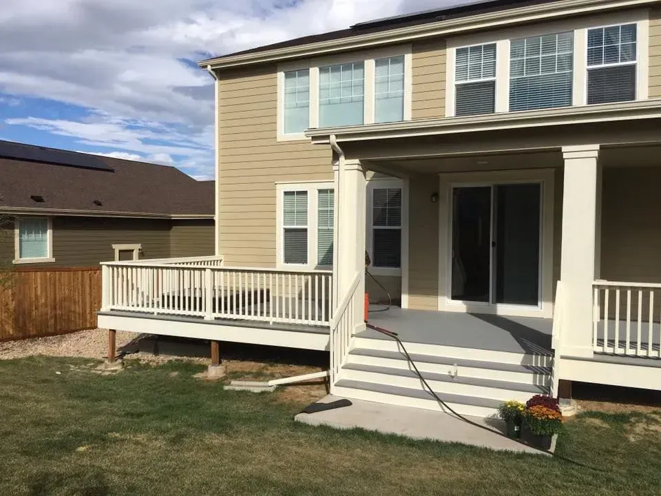 Backyard with a deck, covered patio, and two-story beige house. A brown house and fence are in the background.
