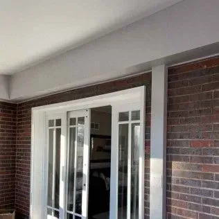 White-framed French doors on a brick wall, under a white roof.