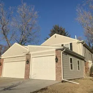Two-story house with attached garages and siding. Blue sky, bare trees, and a driveway.